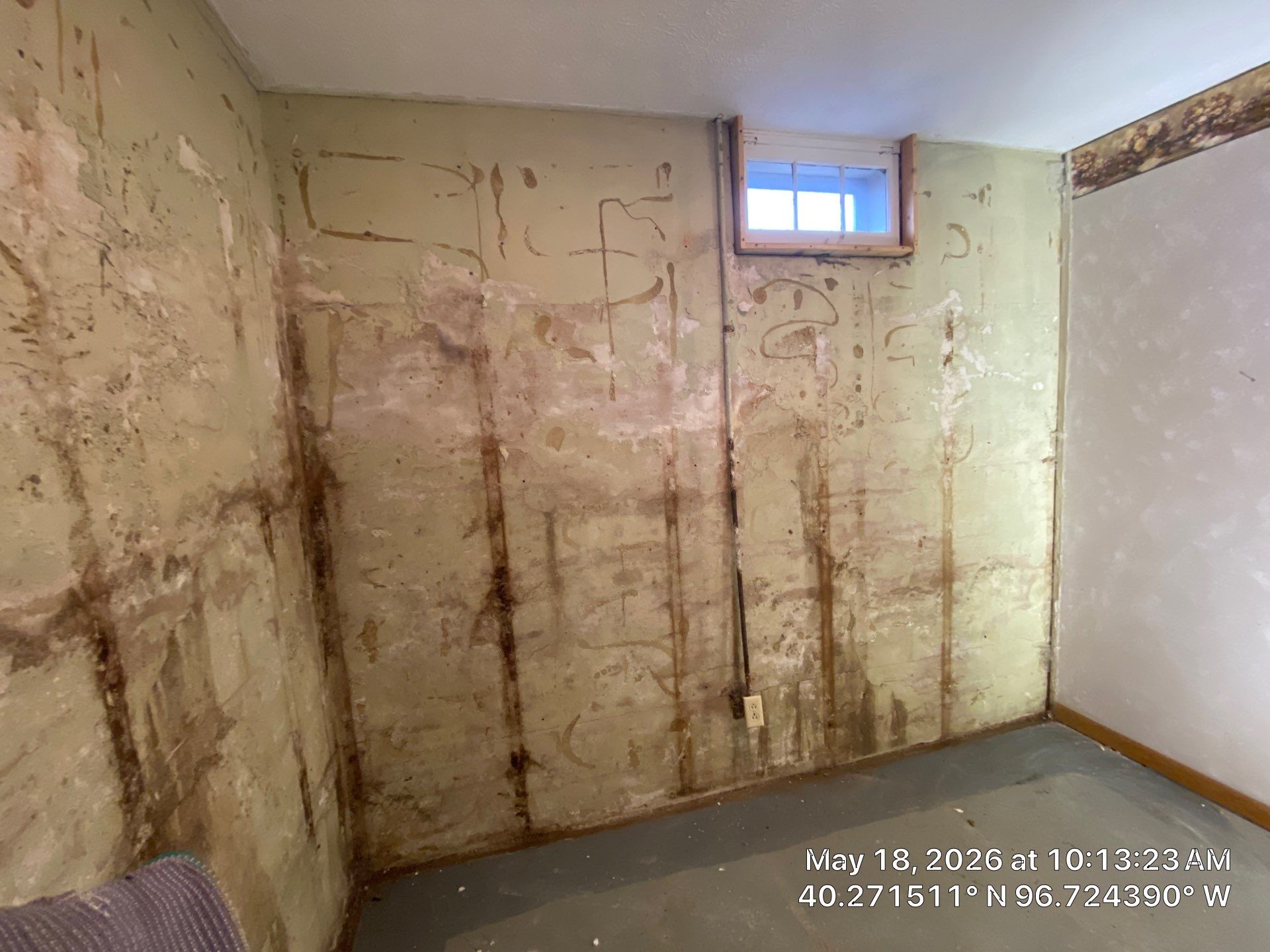 Epp Foundation Repair inspecting extensive water damage and peeling paint on a basement wall in Beatrice, NE